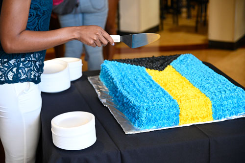 Giana Fernander cuts Bahamas flag cake, baked and decorated by Dining Services